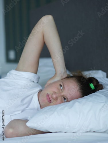 Young sad depressed unhappy worried woman in the bed in bedroom at home in the morning and feel angry neighbors are noisy, lying under white blanket suffer from insomnia problems with sleep at night 