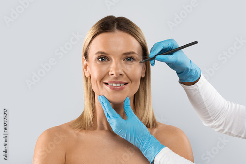 Plastic surgeon drawing lines on middle aged woman face