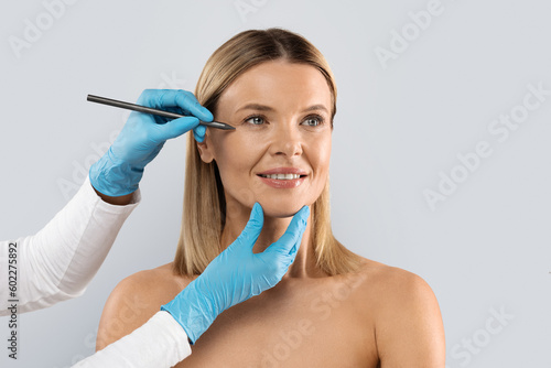 Beautician drawing lines under middle aged woman eyes