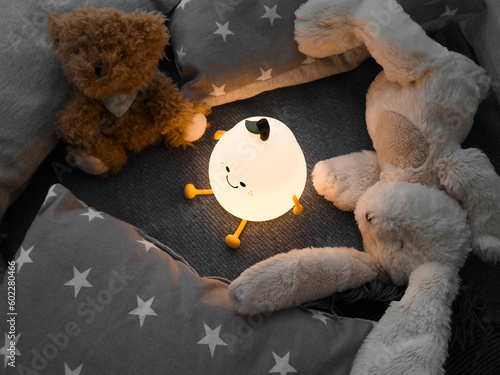 Kids' night light among pillows and toys. Turned on the night light. Cozy shelter for a little toddler. A cute flashlight that illuminates the nursery room.
