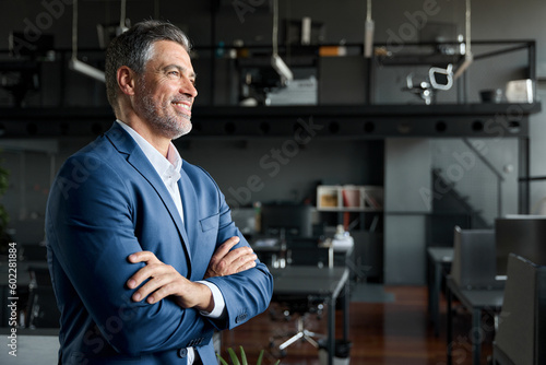 Happy proud prosperous mid aged mature professional business man ceo executive wearing suit standing in office arms crossed looking away thinking of success, leadership, side profile view.