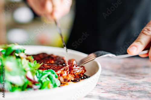 man hands with fork and knife eating beef steak and salad in cafe