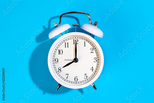 White alarm clock on a blue background isolated, top view.