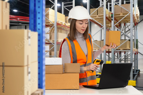 Warehouse specialist woman. Girl storekeeper with scanner. Data collection terminal in worker's hand. Woman among storage boxes and racks. Career in storage industry. Storekeeper using laptop