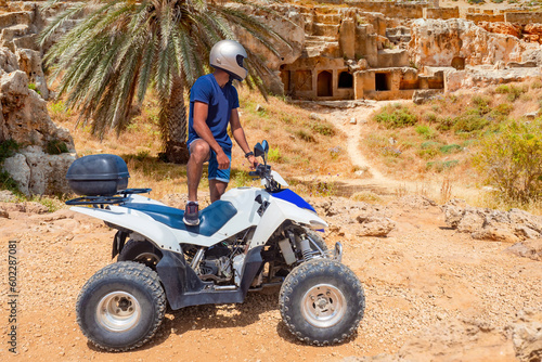 Man with quad bike. Guy travels on atv. Tourist on sandy terrain. Extreme traveler in Cyprus. Atv rider in Paphos. Man with quad bike near archaeological museum. Atv traveler stopped to look around