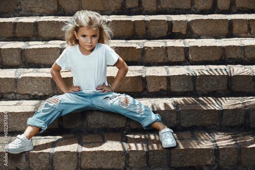 Tableau sur toile A little toddler girl sitting on the stairs and posing in jeans and white shirt