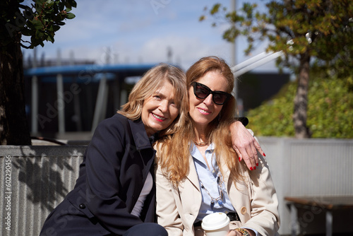 Two women looking at the camera and smiling while posing together outdoors.