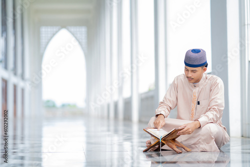  An Asian Muslim man is sitting and reading the Quran. The peace in the mosque makes it an energetic atmosphere of faith, Arabic word translation: The Holy Al Quran.