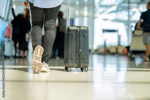 Traveler woman legs walking carrying a suitcase in airport terminal. Copy space