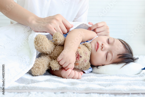 Cute toddle baby girl infant sleeping on white bed, mother  hands covering sleepy little girl daughter with blanket, mom comforting sleeping kid, parent take care child at home, love family.