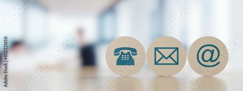 Wooden round telephone, envelope letter and e-mail symbols in a row on wooden table with a blurred office in the background, contact us symbols or banner with copy space