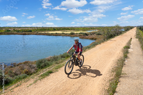 beautiful senior woman cycling with her electric mountain bike on a via verde in the wetlands of Isla Christina, Andalusia, Spain