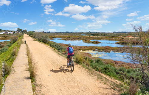 beautiful senior woman cycling with her electric mountain bike on a via verde in the wetlands of Isla Christina, Andalusia, Spain