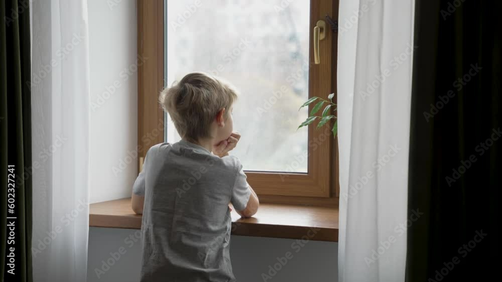 Boy is looking out of the window. Teenager stays next to window at home alone and is sad or thinking about something. Emotional concept Boy is looking out of the window. Teenager stays next to window at home alone and is sad or thinking about something. Emotional concept