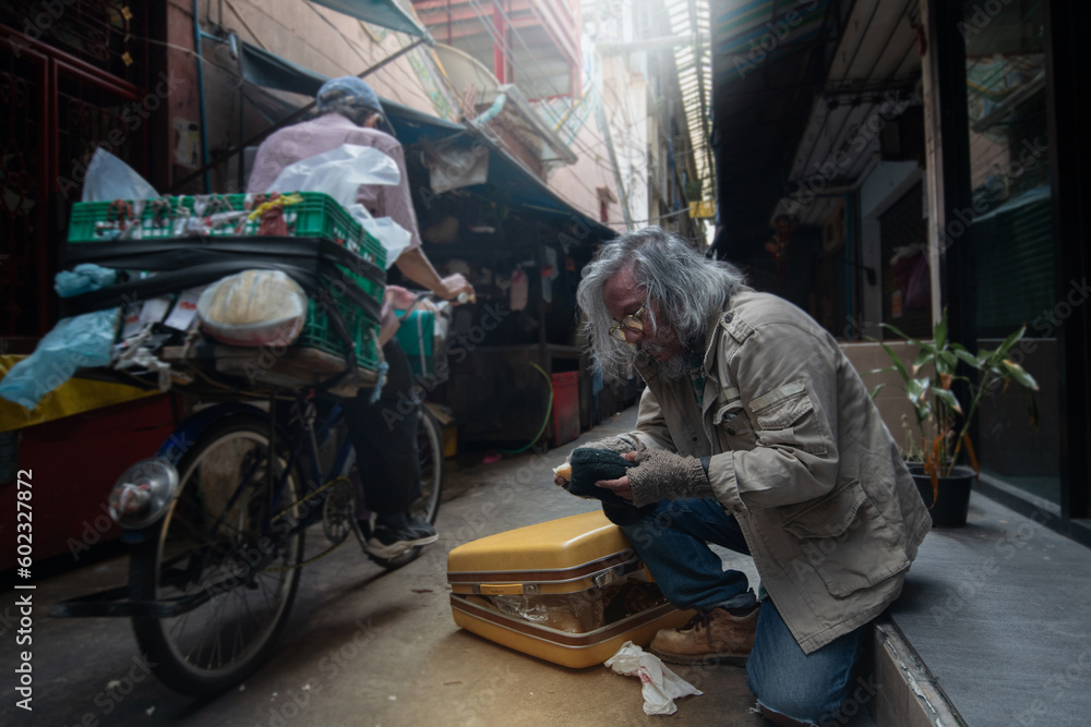Homeless old man in narrow and dirty alley, with large luggage, unemployment and homeless people concept