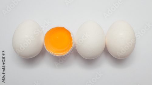 Row of white eggs and single broken egg with a yolk.
