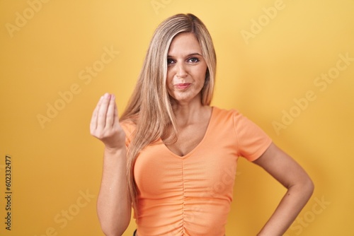 Young woman standing over yellow background doing italian gesture with hand and fingers confident expression