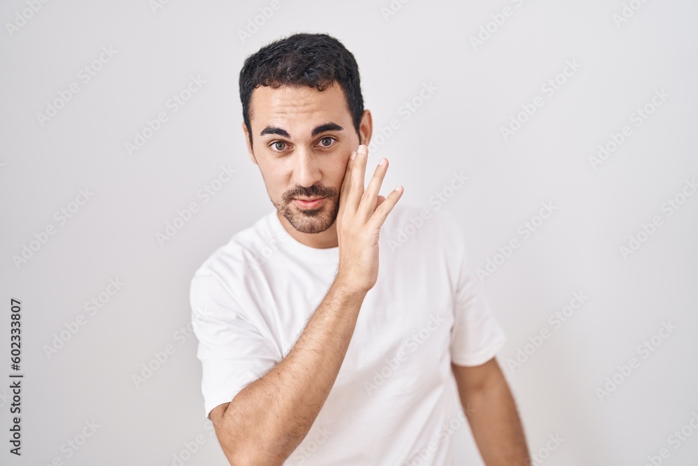 Handsome hispanic man standing over white background hand on mouth telling secret rumor, whispering malicious talk conversation Handsome hispanic man standing over white background hand on mouth telling secret rumor, whispering malicious talk conversation
