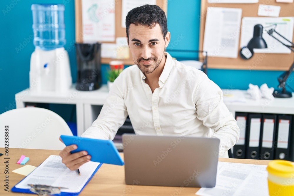 Young hispanic man business worker using laptop and touchpad working at office Young hispanic man business worker using laptop and touchpad working at office