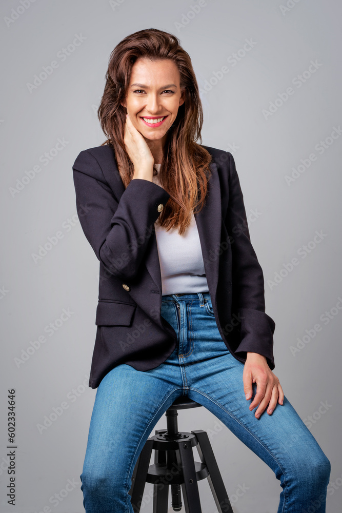 Portrait of an attractive brunette haired woman sitting at isolated dark background