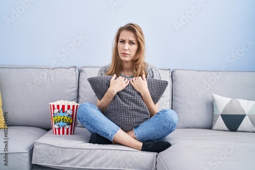 Beautiful blonde woman watching tv sitting on the sofa skeptic and nervous, frowning upset because of problem. negative person.