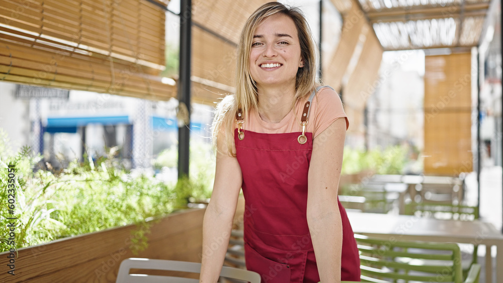 Young blonde woman waitress smiling confident standing at coffee shop terrace