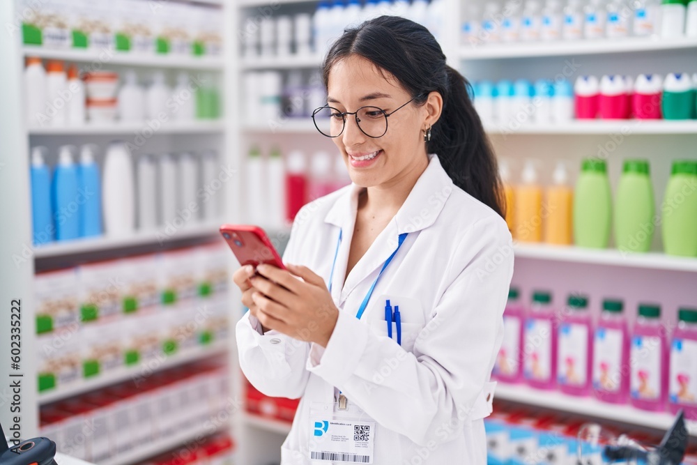 Young beautiful hispanic woman pharmacist using smartphone working at pharmacy