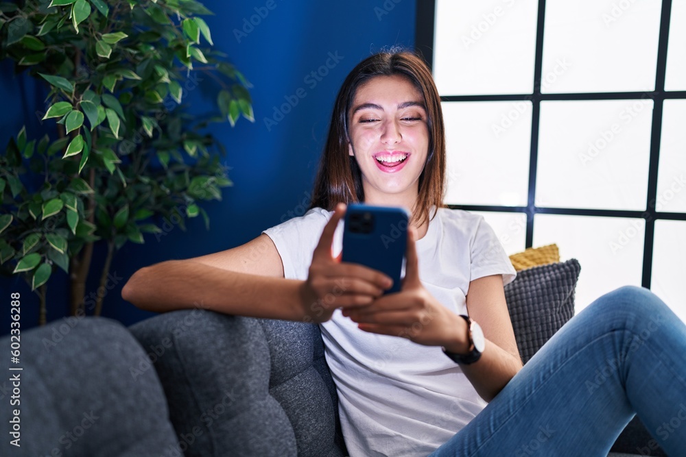 Young beautiful hispanic woman using smartphone sitting on sofa at home Young beautiful hispanic woman using smartphone sitting on sofa at home