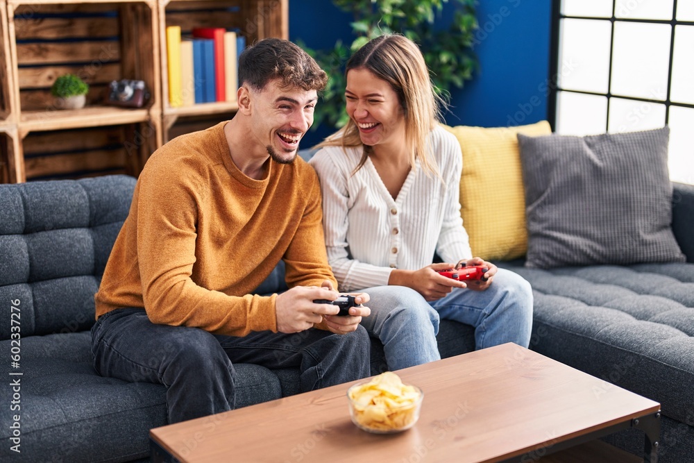 Young man and woman couple playing video game sitting on sofa at home Young man and woman couple playing video game sitting on sofa at home