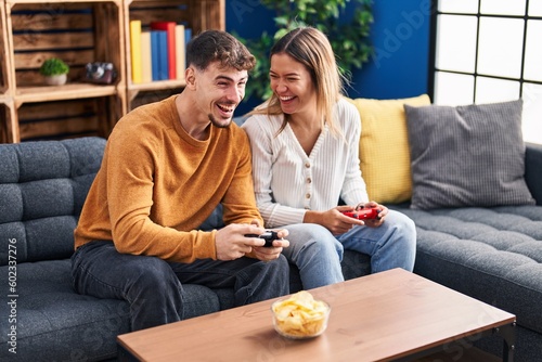 Young man and woman couple playing video game sitting on sofa at home