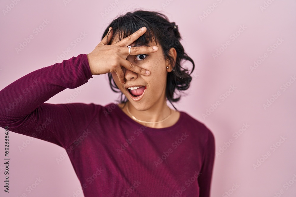 Young beautiful woman standing over pink background peeking in shock covering face and eyes with hand, looking through fingers with embarrassed expression. Young beautiful woman standing over pink background peeking in shock covering face and eyes with hand, looking through fingers with embarrassed expression.