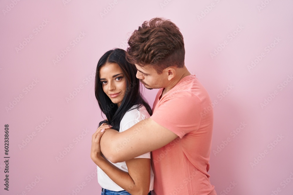 Young hispanic couple standing over pink background looking to side, relax profile pose with natural face and confident smile. Young hispanic couple standing over pink background looking to side, relax profile pose with natural face and confident smile.