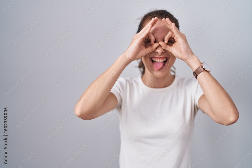Beautiful brunette woman standing over isolated background doing ok gesture like binoculars sticking tongue out, eyes looking through fingers. crazy expression. Beautiful brunette woman standing over isolated background doing ok gesture like binoculars sticking tongue out, eyes looking through fingers. crazy expression.