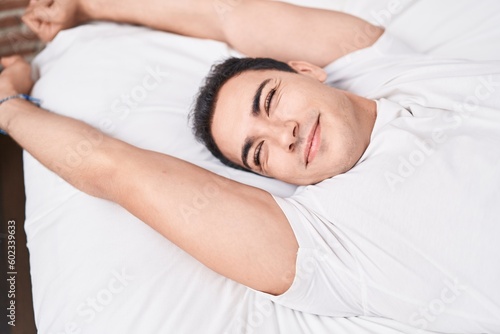 Young hispanic man waking up stretching arms at bedroom