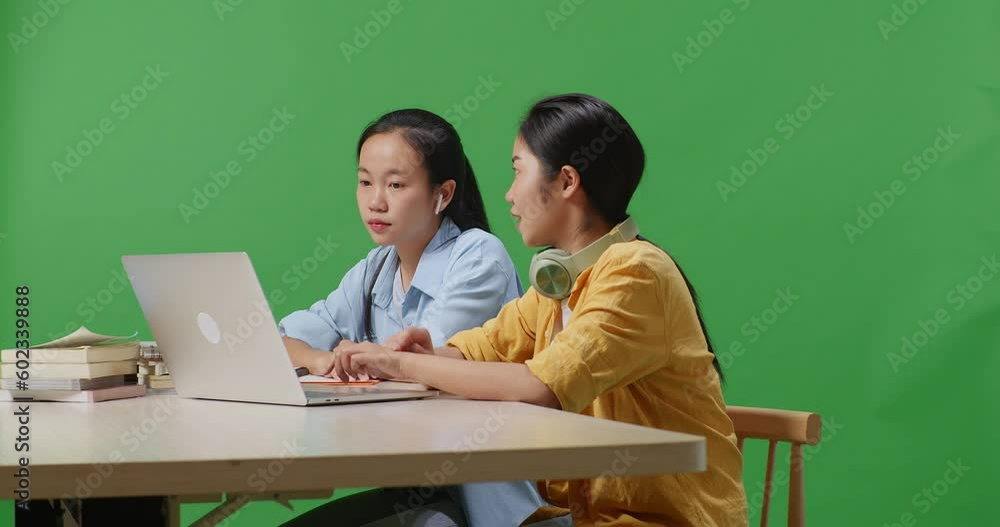 Asian Woman Student Teaching Her Friend On A Laptop While Sitting On A Table In The Green Screen Background Classroom
