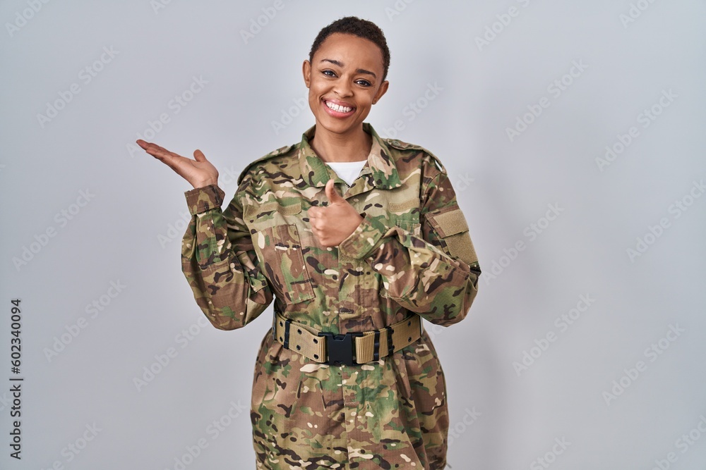 Beautiful african american woman wearing camouflage army uniform showing palm hand and doing ok gesture with thumbs up, smiling happy and cheerful