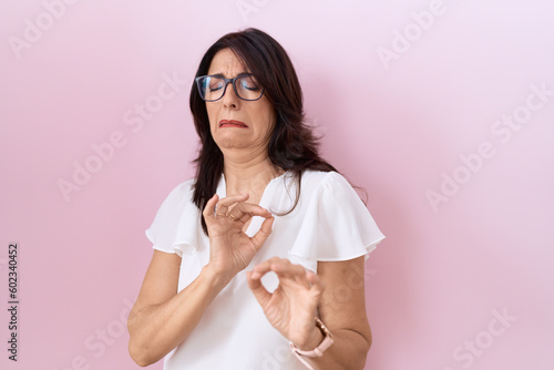 Obraz na płótnie Middle age hispanic woman wearing casual white t shirt and glasses disgusted expression, displeased and fearful doing disgust face because aversion reaction