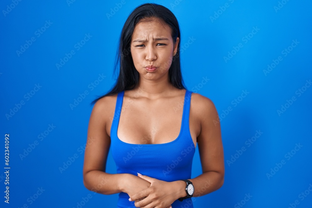 Hispanic woman standing over blue background puffing cheeks with funny face. mouth inflated with air, crazy expression.