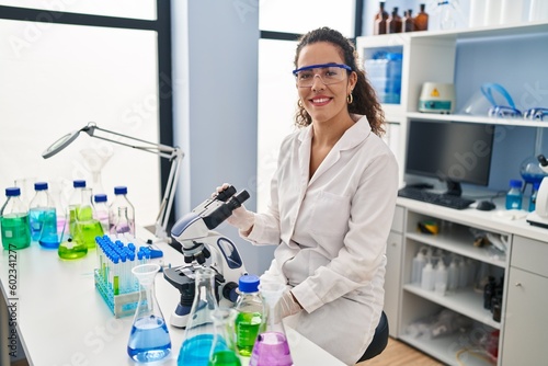 Young hispanic woman working at scientist laboratory looking positive and happy standing and smiling with a confident smile showing teeth