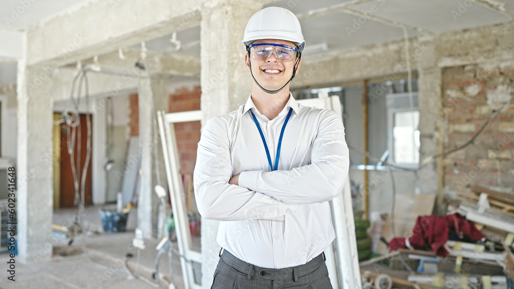 Young hispanic man architect smiling confident standing with arms crossed gesture at construction site