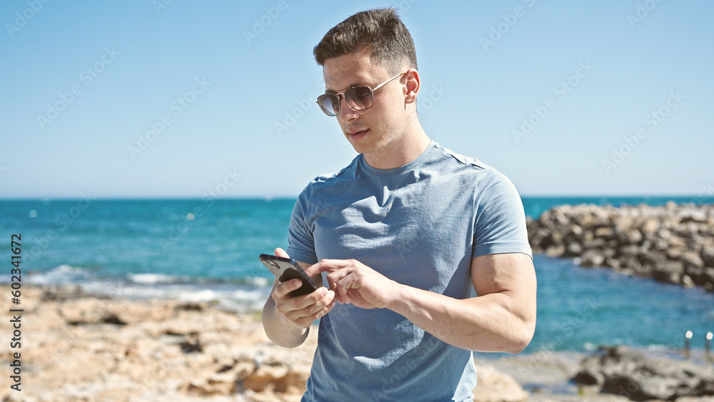 Young hispanic man tourist using smartphone with relaxed expression at seaside Young hispanic man tourist using smartphone with relaxed expression at seaside