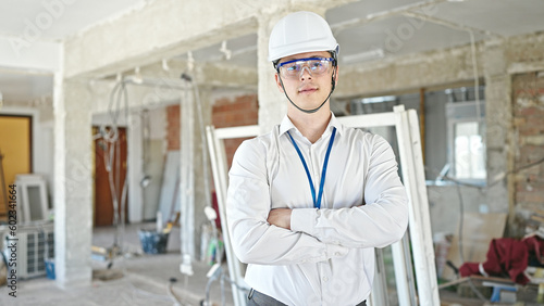 Young hispanic man architect standing with relaxed expression and arms crossed gesture at construction site