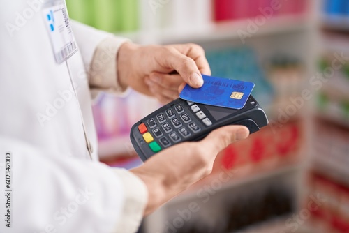 Young caucasian man pharmacist using credit card and data phone at pharmacy