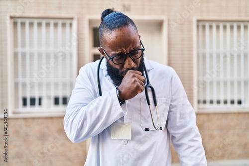 African american man wearing doctor uniform and stethoscope feeling unwell and coughing as symptom for cold or bronchitis. health care concept.