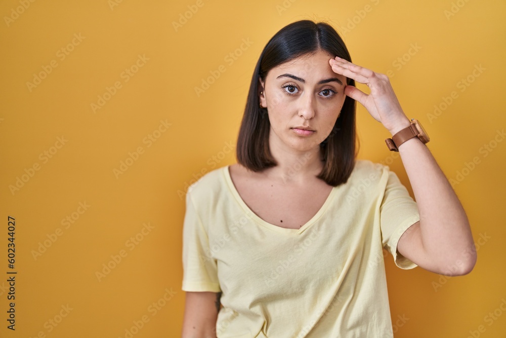Hispanic girl wearing casual t shirt over yellow background worried and stressed about a problem with hand on forehead, nervous and anxious for crisis Hispanic girl wearing casual t shirt over yellow background worried and stressed about a problem with hand on forehead, nervous and anxious for crisis