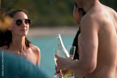 Man and woman friends group enjoy celebration party and fun luxury summer outdoor lifestyle by drinking champagne together, travel vacation on catamaran yacht boat sailing in tropical sea sunset on © chokniti