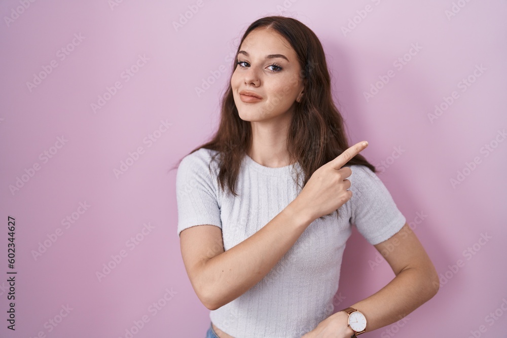 Young hispanic girl standing over pink background pointing with hand finger to the side showing advertisement, serious and calm face Young hispanic girl standing over pink background pointing with hand finger to the side showing advertisement, serious and calm face
