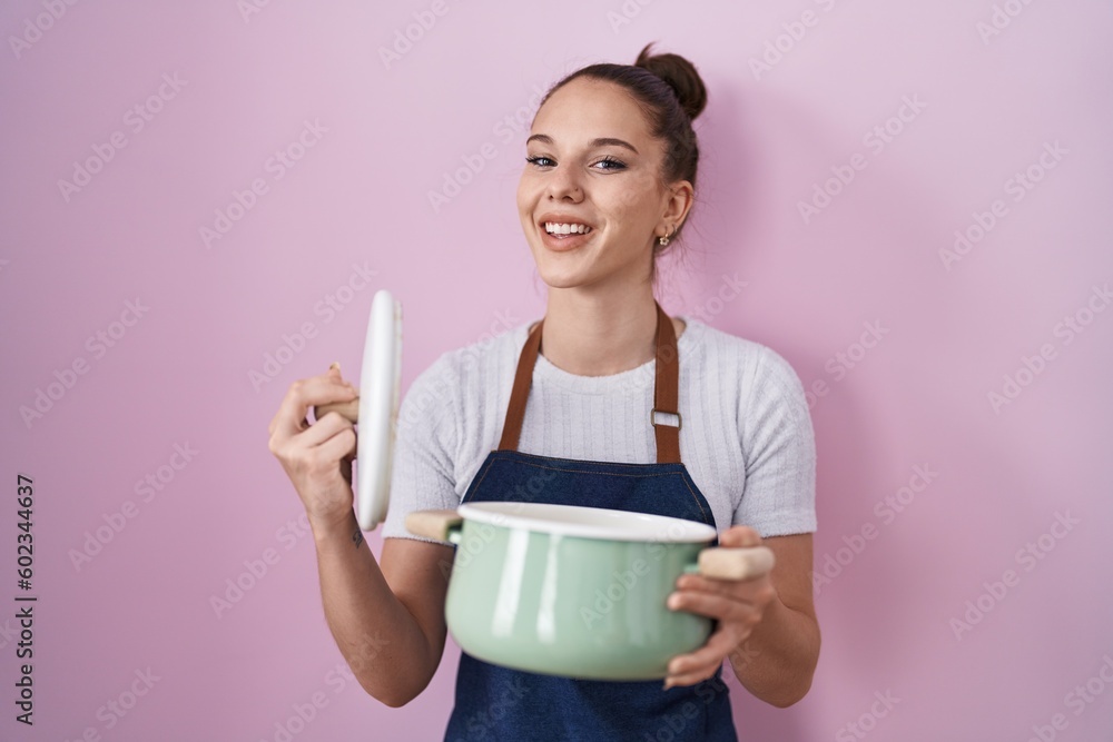 Young hispanic girl wearing apron holding cooking pot smiling and laughing hard out loud because funny crazy joke. Young hispanic girl wearing apron holding cooking pot smiling and laughing hard out loud because funny crazy joke.