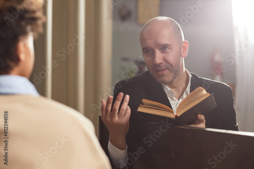 Фотография Mature pastor reading Bible and talking to boy during their meeting in church