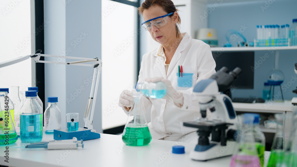 Middle age hispanic woman wearing scientist uniform pouring liquid on test tube at laboratory Middle age hispanic woman wearing scientist uniform pouring liquid on test tube at laboratory